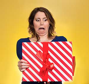 Image of a brunette woman, wearing a blue dress, with an appalled facial expressing, holding a red and white striped gift