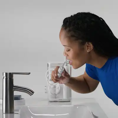 Woman in a bathroom using a Waterpik water flosser