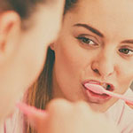 Woman brushing teeth, looking in mirror