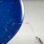 Blue balloon with the words Powerful Yet Gentle! with a Waterpik™ water flosser handle and tip shooting water against it