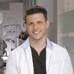 Photo of Dr. Chris Strandburg, indoors in his dental office, with short brown hair, wearing a white lab coat and black shirt